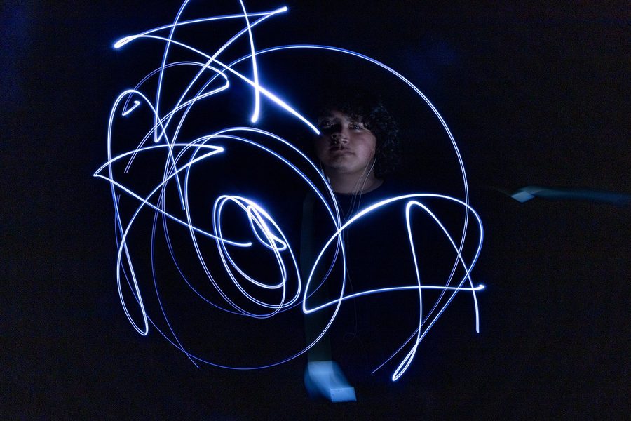 Dense scribbles of light across a dark frame, a face glowing behind them